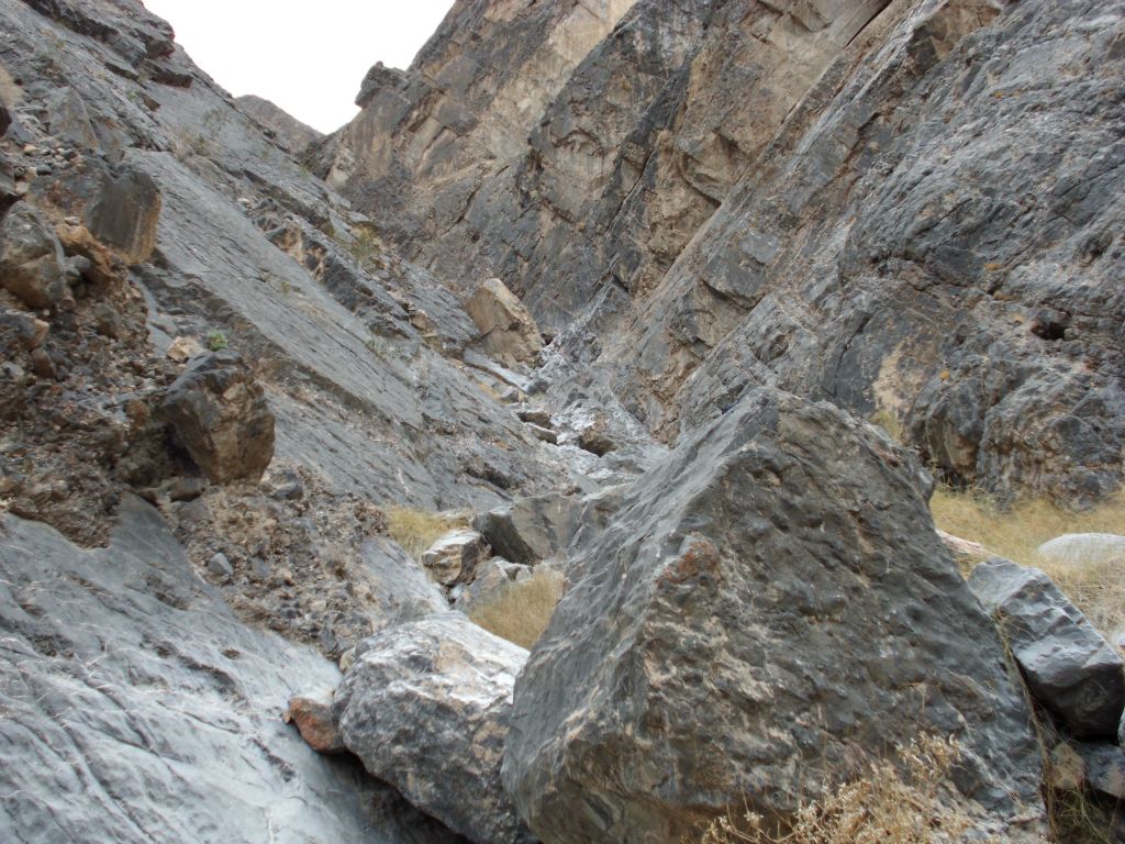 A very narrow wash with diagonal walls sloping down from both sides of the canyon: