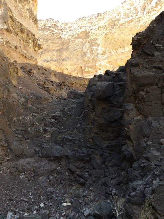 Climbing a gently sloped dry fall with the sun creating bright glows on the canyon wall behind: