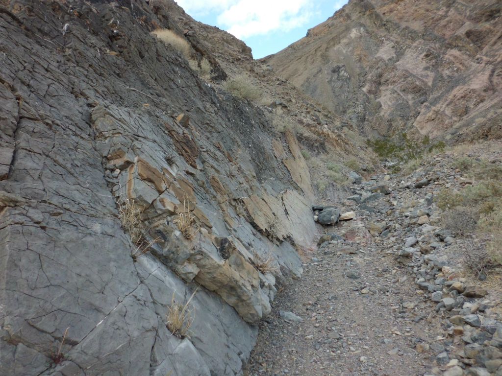Passing through a smooth narrow wash next to a sloped rock wall: