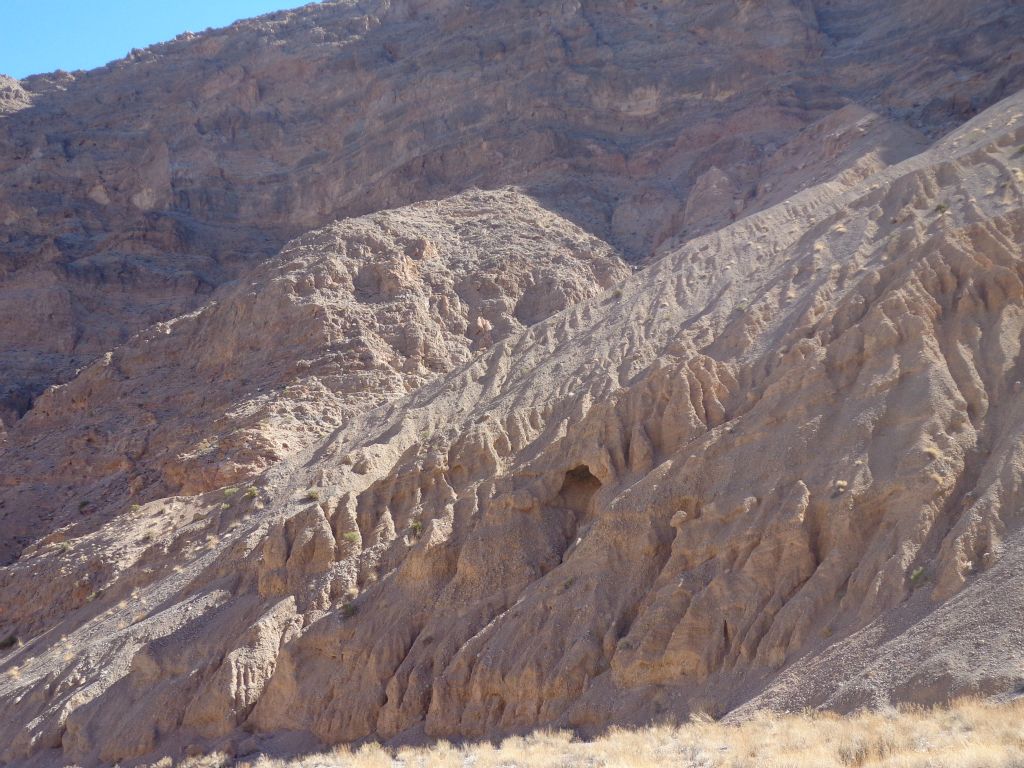 Fluted mud cliffs with a small cave in the middle: